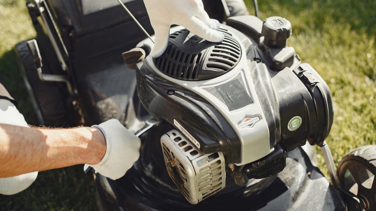 Gloved hands working on a walk-behind lawn mower engine outdoors