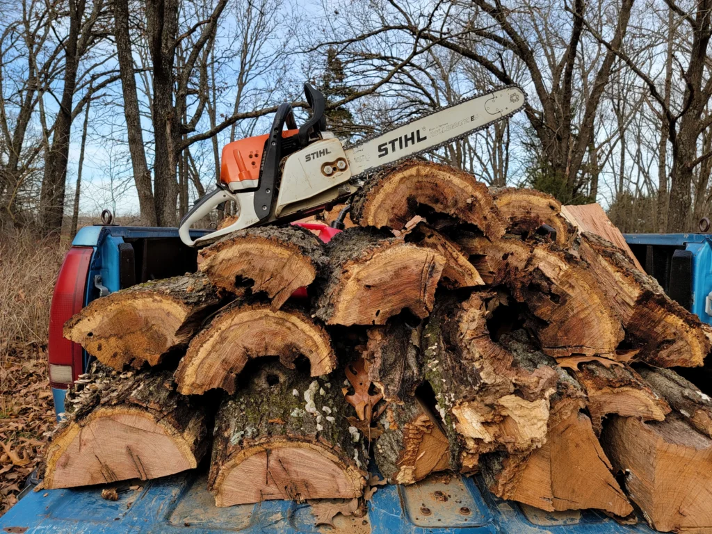Chainsaw resting on a truck bed loaded with fresh-cut firewood rounds